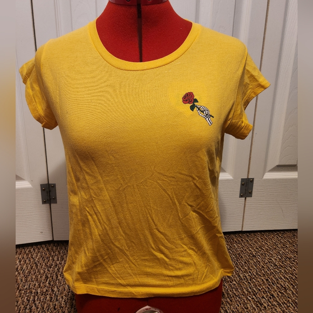 Yellow t shirt with a symbol of a skeleton hand holding a rose